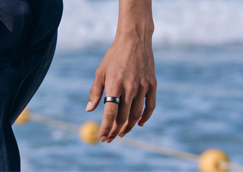 Samsung Galaxy Ring worn on hand near water with swim buoys in the background